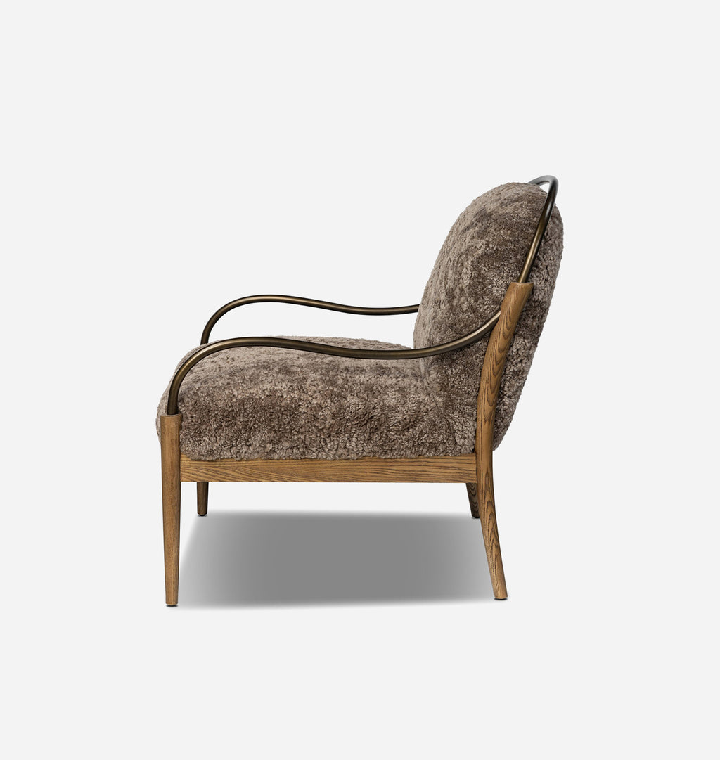 A mid-century modern accent chair featuring textured taupe shearling upholstery, a natural oak wood frame, and a curved black metal armrest.
