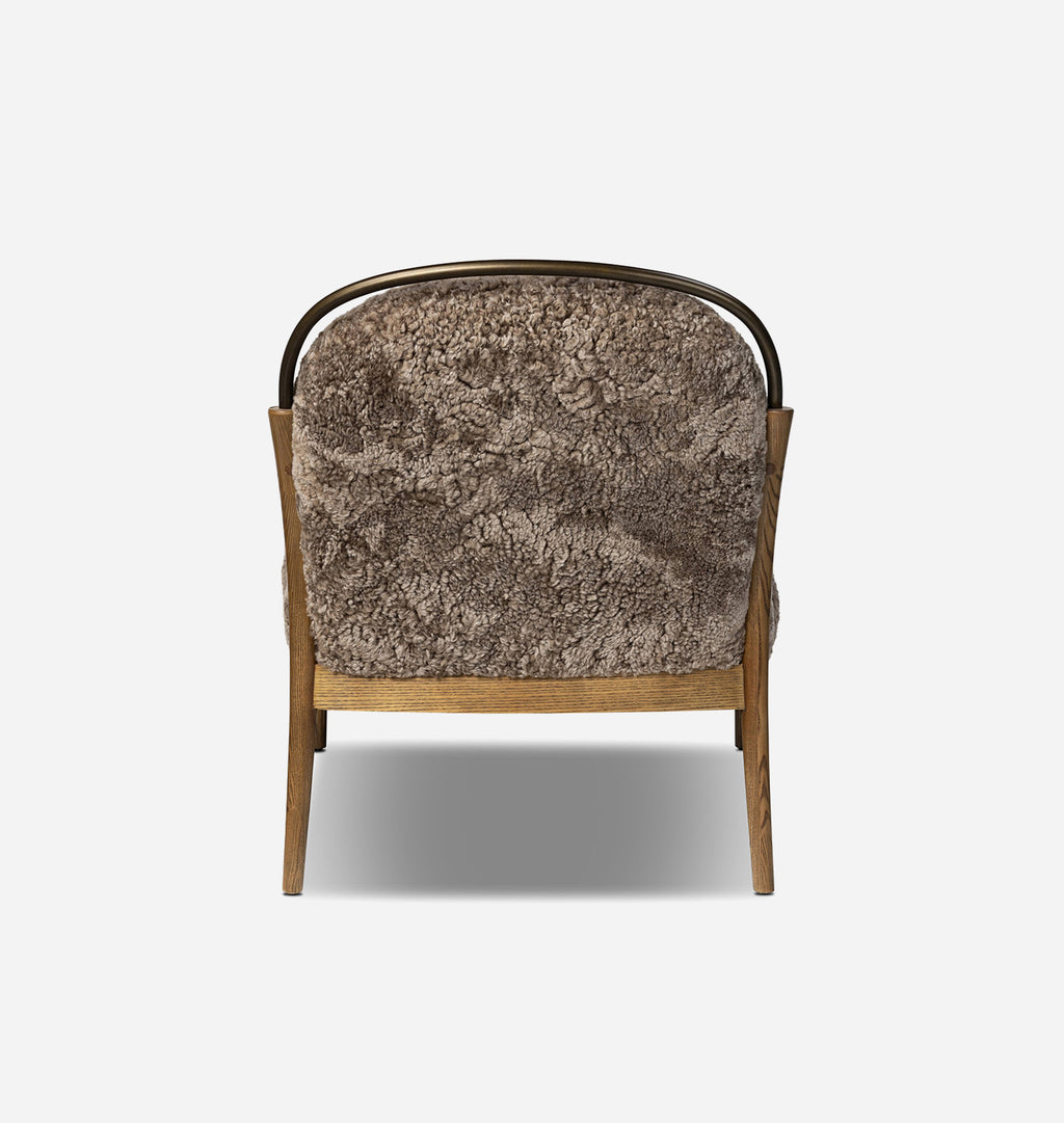 A modern lounge chair viewed from the back, featuring a textured brown shaggy fur cushion, a curved black metal top rail, and a light brown wooden frame on a white background.