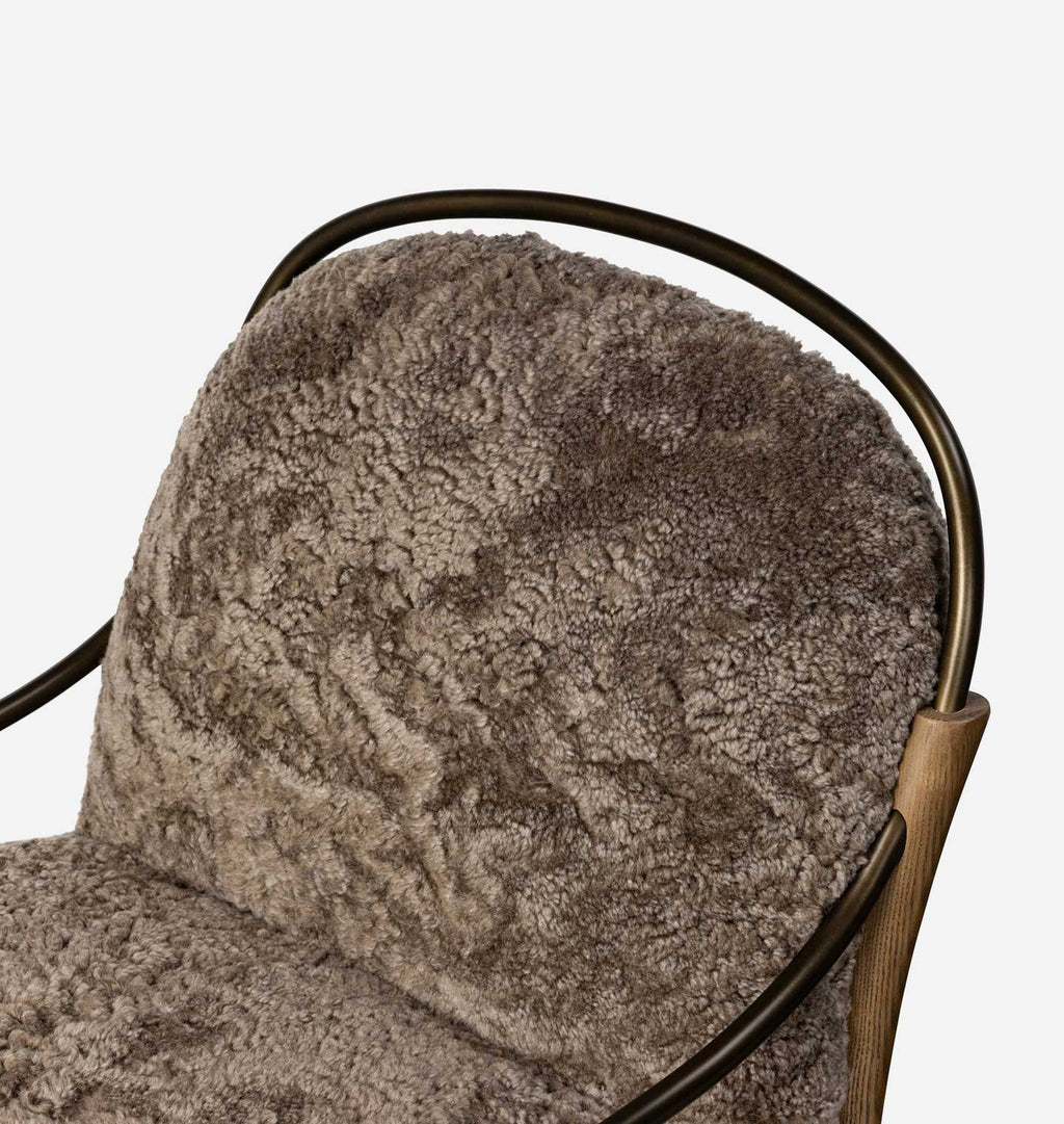 Close-up of a plush, textured taupe-brown sheepskin or faux fur chair cushion, showing the rich pile texture and the dark metal frame.
