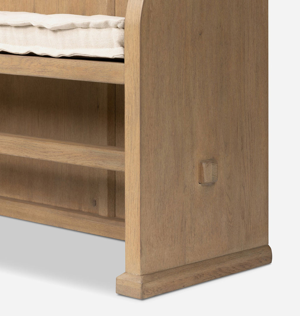 Close-up of a light oak wood bench or bed frame corner with a cream cushion, showing the wooden post, footboard edge, and shelf.