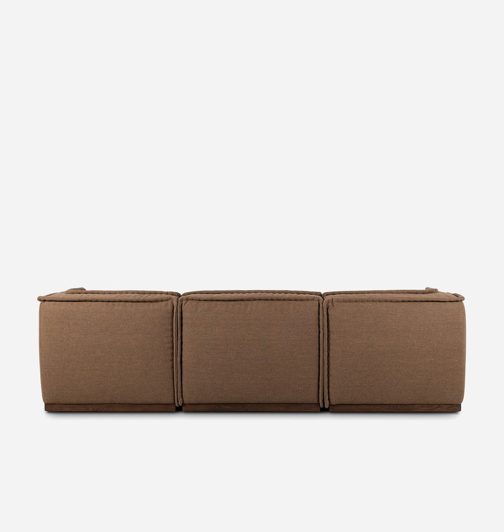 A three-seater upholstered sofa or ottoman in a warm brown fabric, shown from a back view perspective against a solid off-white background.