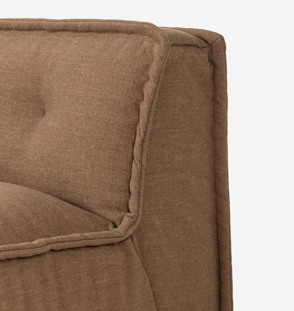 Close-up detail of a brown upholstered chair with tufted cushioning and decorative piping on a light gray background.