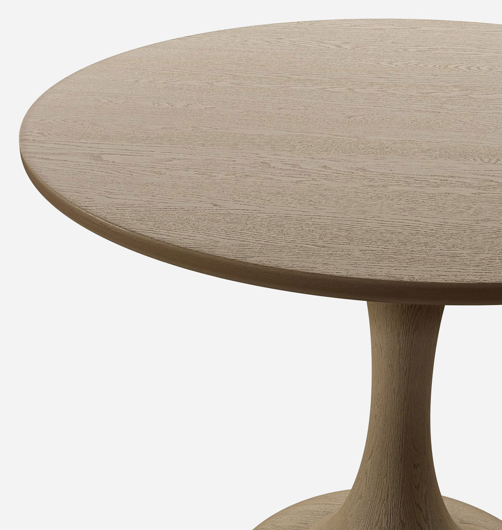 Close-up of a round wooden table with a natural oak finish and a single pedestal base, shown against a plain light background.