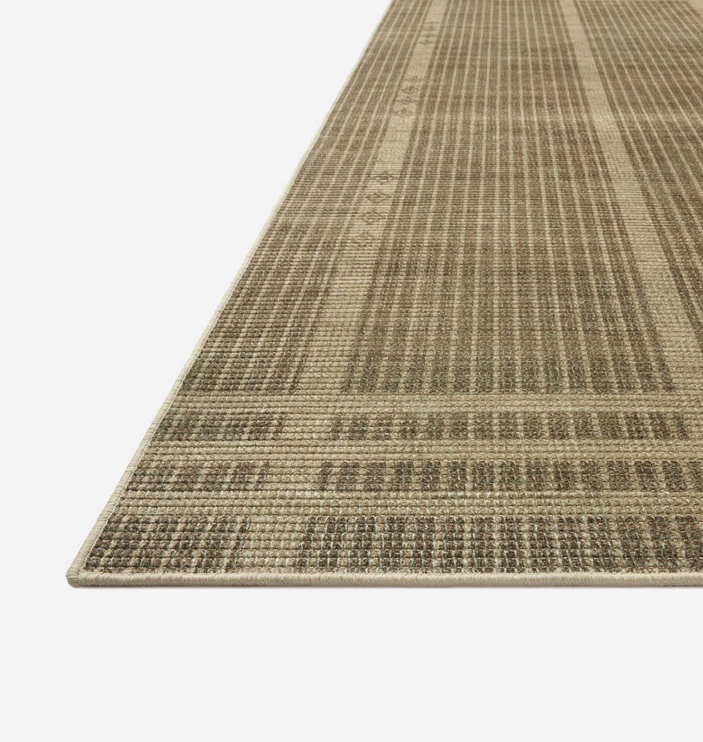 A close-up view of a textured area rug with a woven geometric pattern in shades of beige and brown, shown on a clean white background.