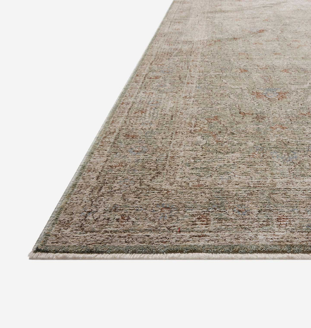 A close-up view of an area rug corner showing its textured, distressed pattern in muted beige, gray, and brown tones on a white background.