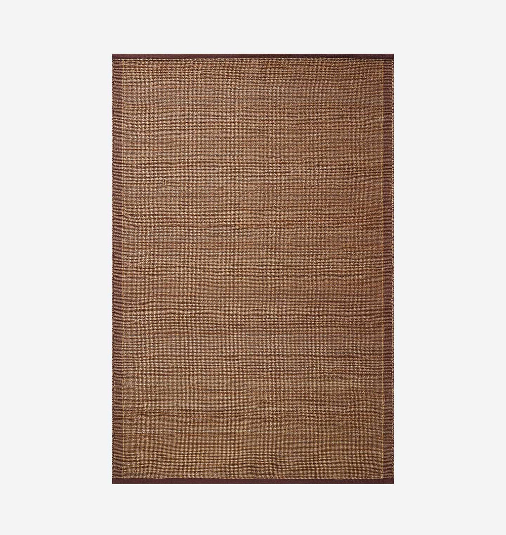 A rectangular woven area rug in a warm medium brown color, featuring a subtle textured weave and a darker brown border, shown flat against a light gray background.