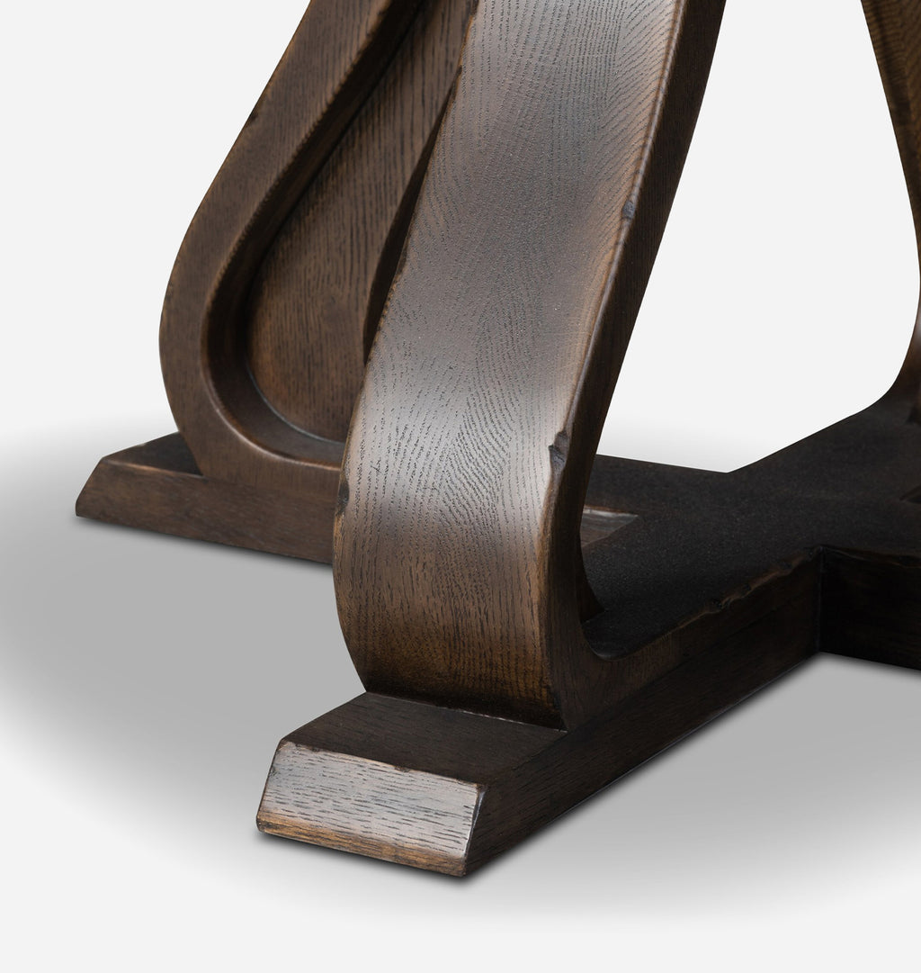 Close-up of a dark brown wooden table base with sculptural curved legs and block feet, photographed on a light gray studio background.