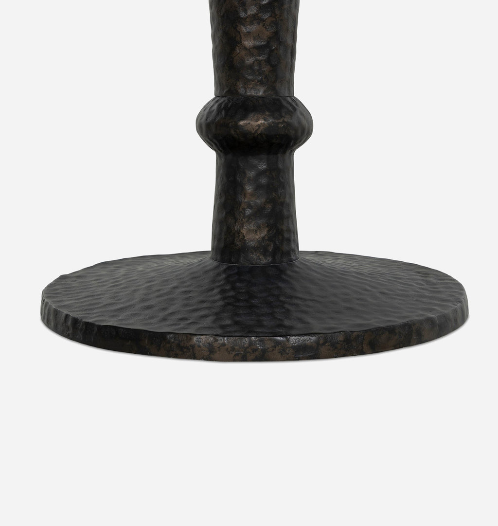 Close-up of a dark hammered metal table base with a circular footplate and a textured central stem, shown on a light gray background.