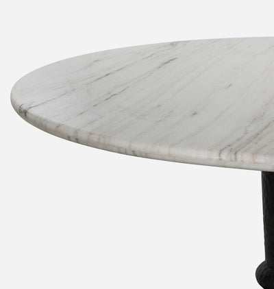 Close-up of a round dining table with a white marble top featuring subtle gray veining and a dark pedestal base, shown against a plain white background.