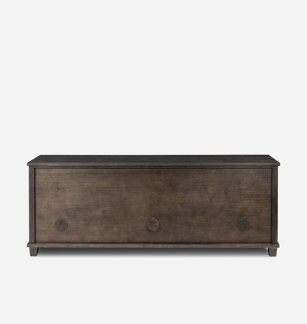 A back view of a  rustic dark brown wooden media console with three drawers and round cord cut outs, shown against a plain light gray background.