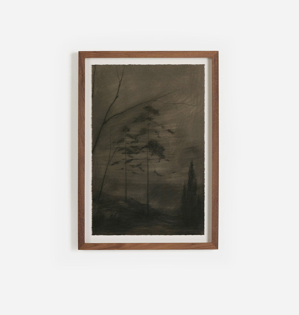 A framed dark monochrome landscape artwork with silhouetted trees, mounted on a white wall in a medium brown wooden frame.