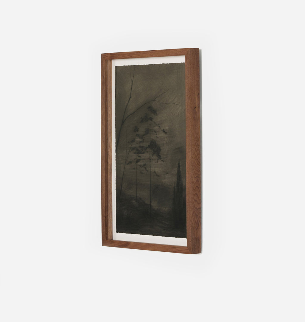 A framed vertical art print featuring a dark, moody forest scene with tall trees in muted brown, gray, and black tones, set in a medium brown wooden frame with a white mat, shown against a plain white wall.