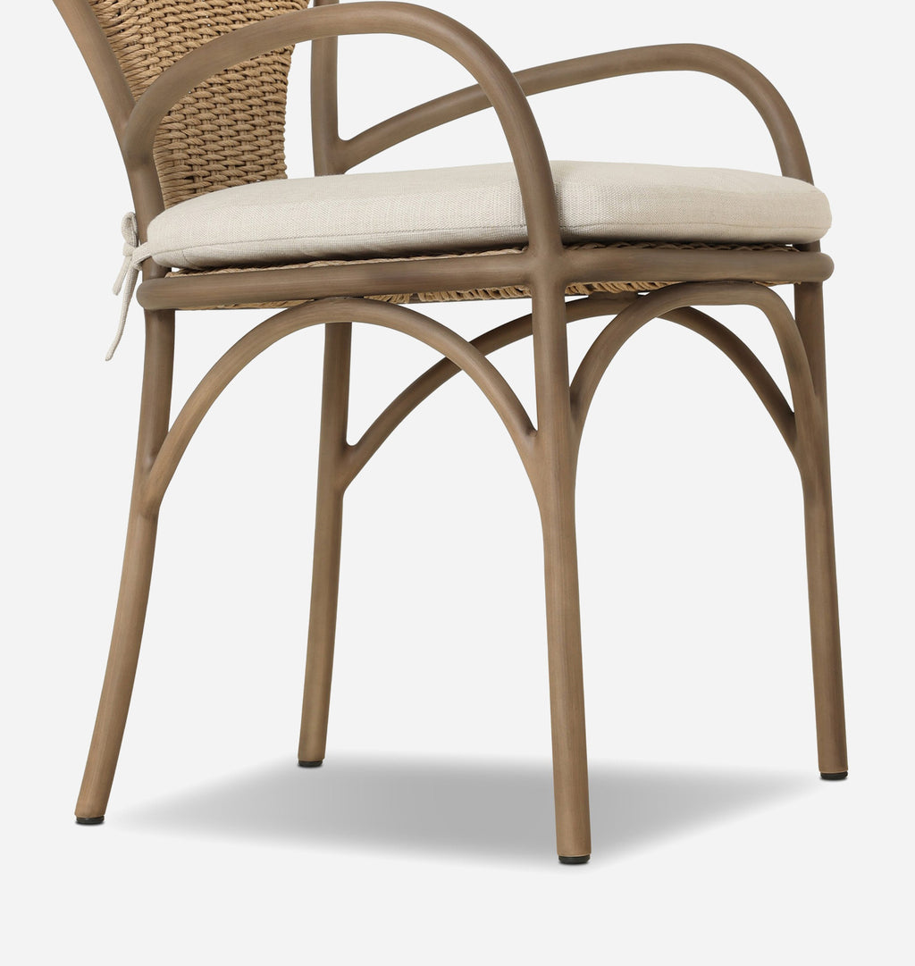 A close-up of a dining chair featuring a curved taupe-brown metal frame, woven wicker backrest, and a light beige fabric seat cushion.