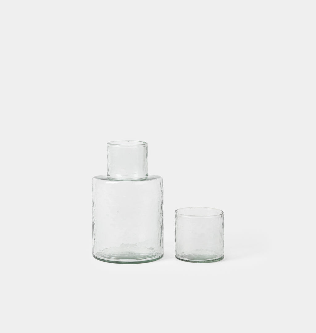 Two clear textured glass vessels, one larger bottle with a short neck and one smaller tumbler, on a light gray background.