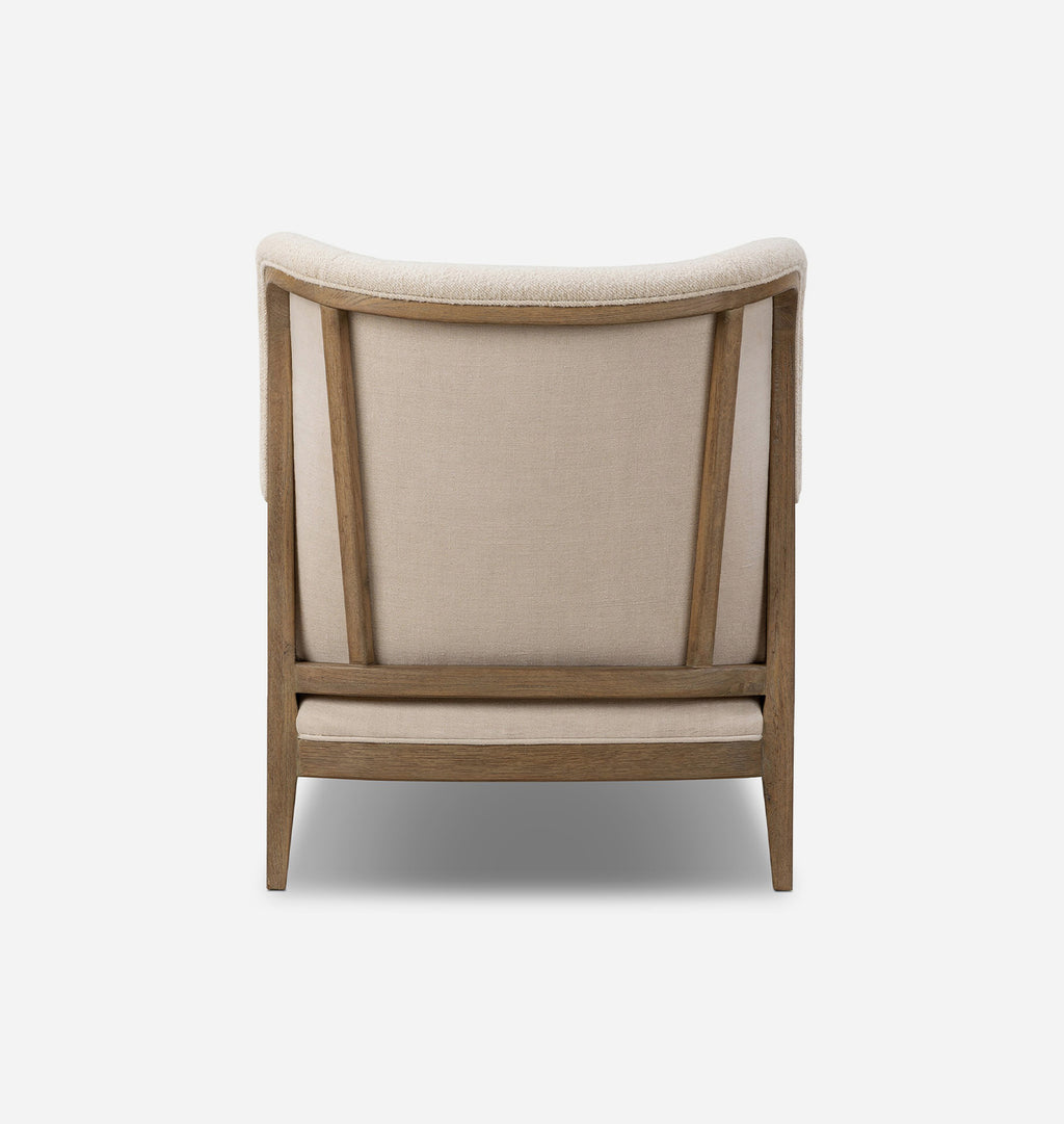 A modern accent chair with a curved backrest, upholstered in a warm beige fabric and supported by a light brown wooden frame, shown from the back against a plain white background.