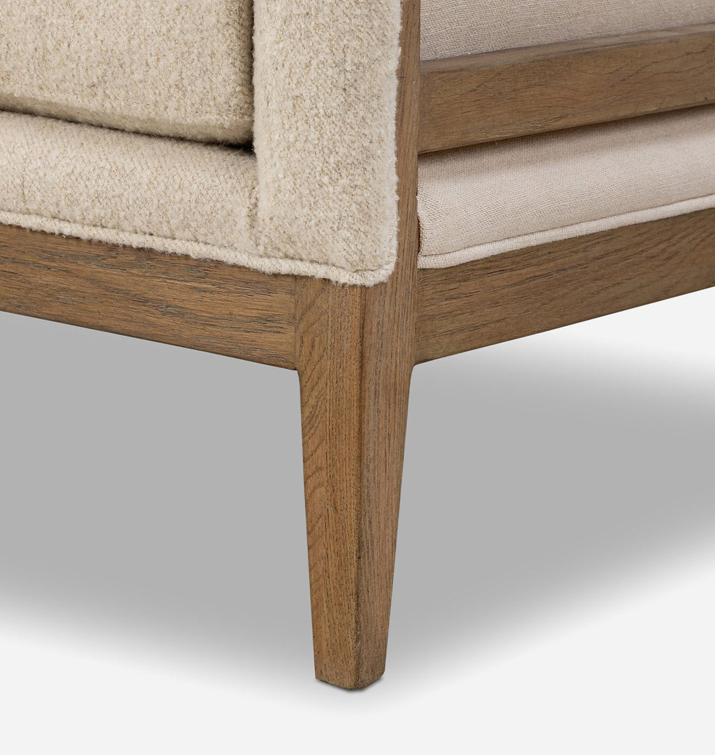 Close-up detail of a mid-century modern armchair corner, showing a warm medium-brown wooden frame and textured cream bouclé upholstery.