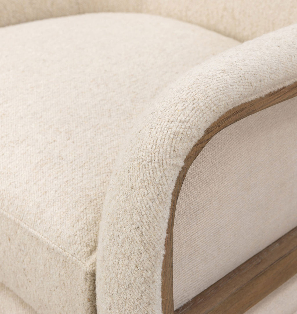 Close-up detail of a cream-colored upholstered armchair with a textured bouclé fabric and a curved wooden frame.