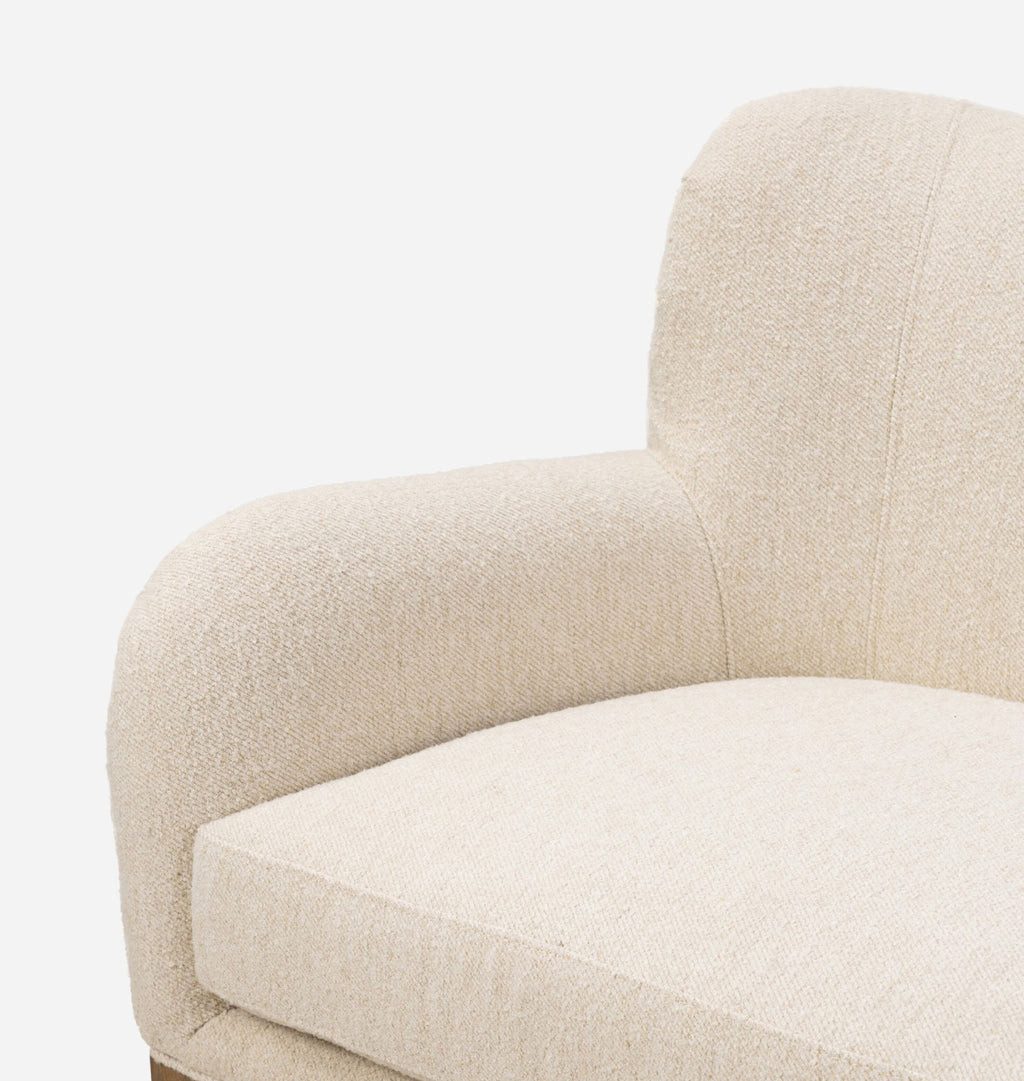 Close-up of a cream-colored bouclé upholstered armchair showing the textured fabric and curved armrest against a plain white background.