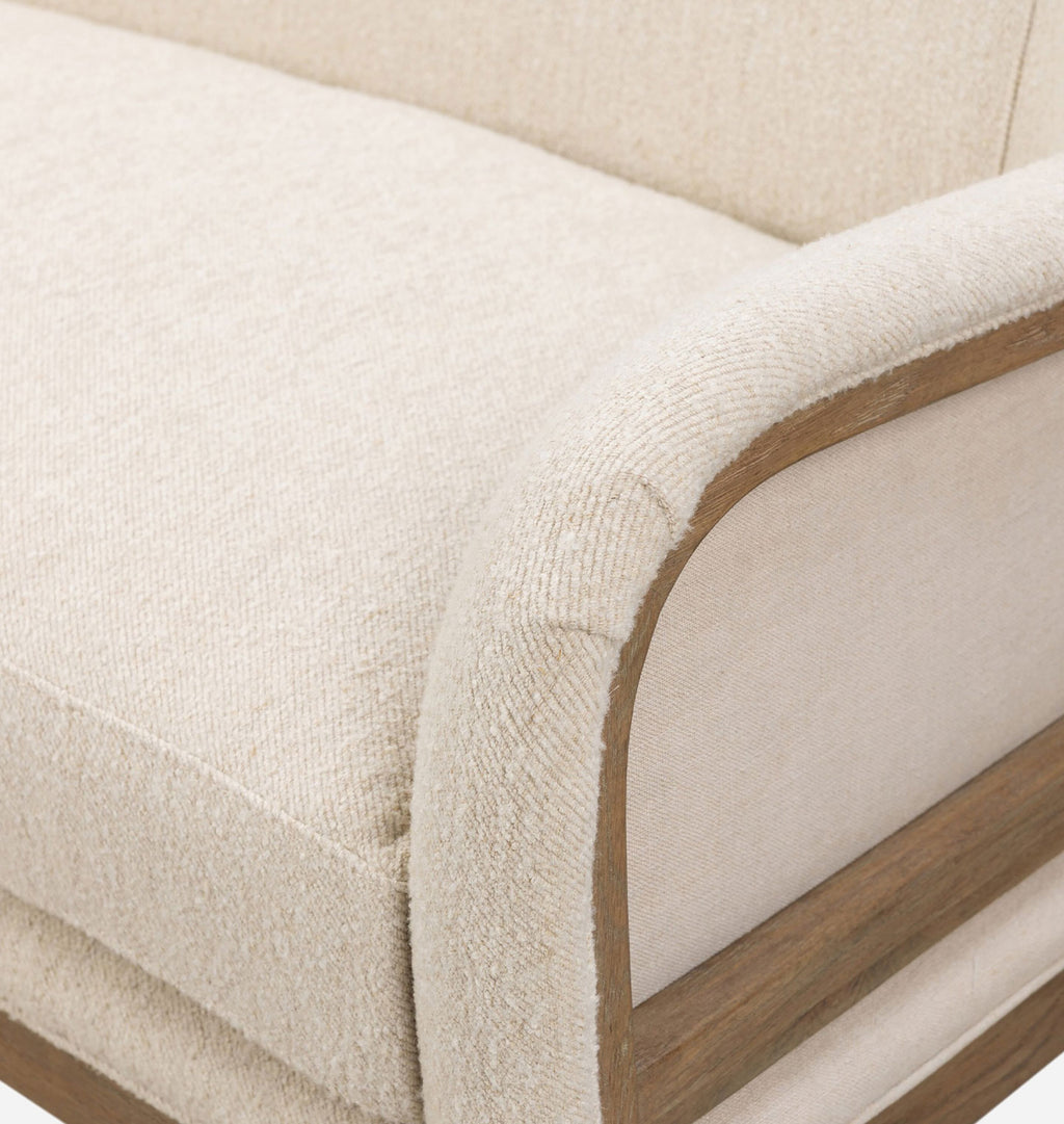 Close-up of a sofa corner showing textured cream upholstery, a curved wooden armrest frame, and a light neutral background.