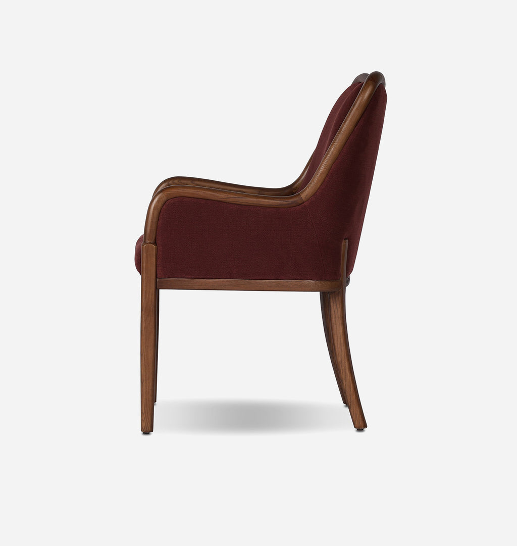 A side-view shot of an armchair with deep burgundy velvet upholstery and a medium brown wooden frame, set against a plain light gray background.