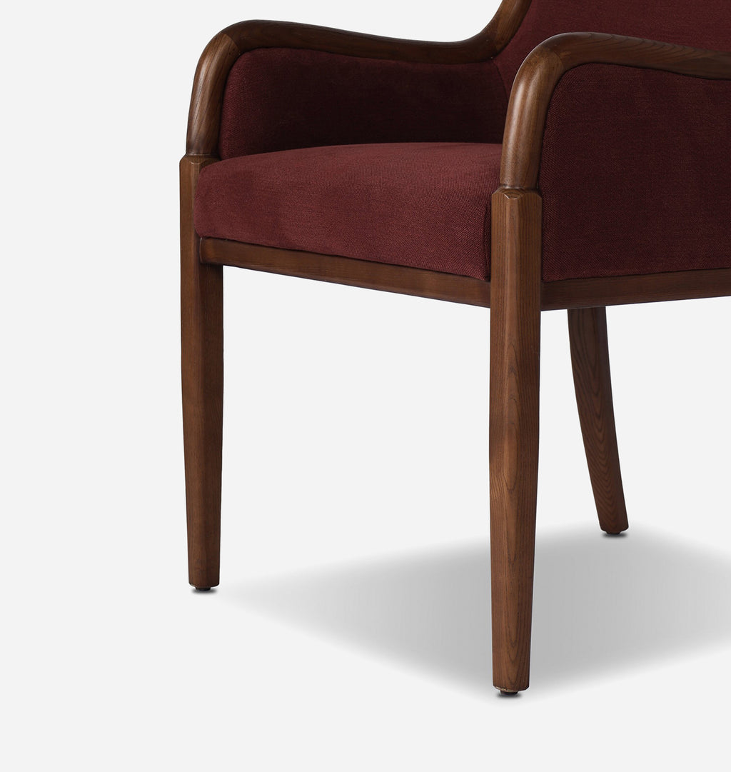 A close-up of a modern armchair featuring deep burgundy velvet upholstery and a medium brown wooden frame with tapered legs, shown against a light gray background.