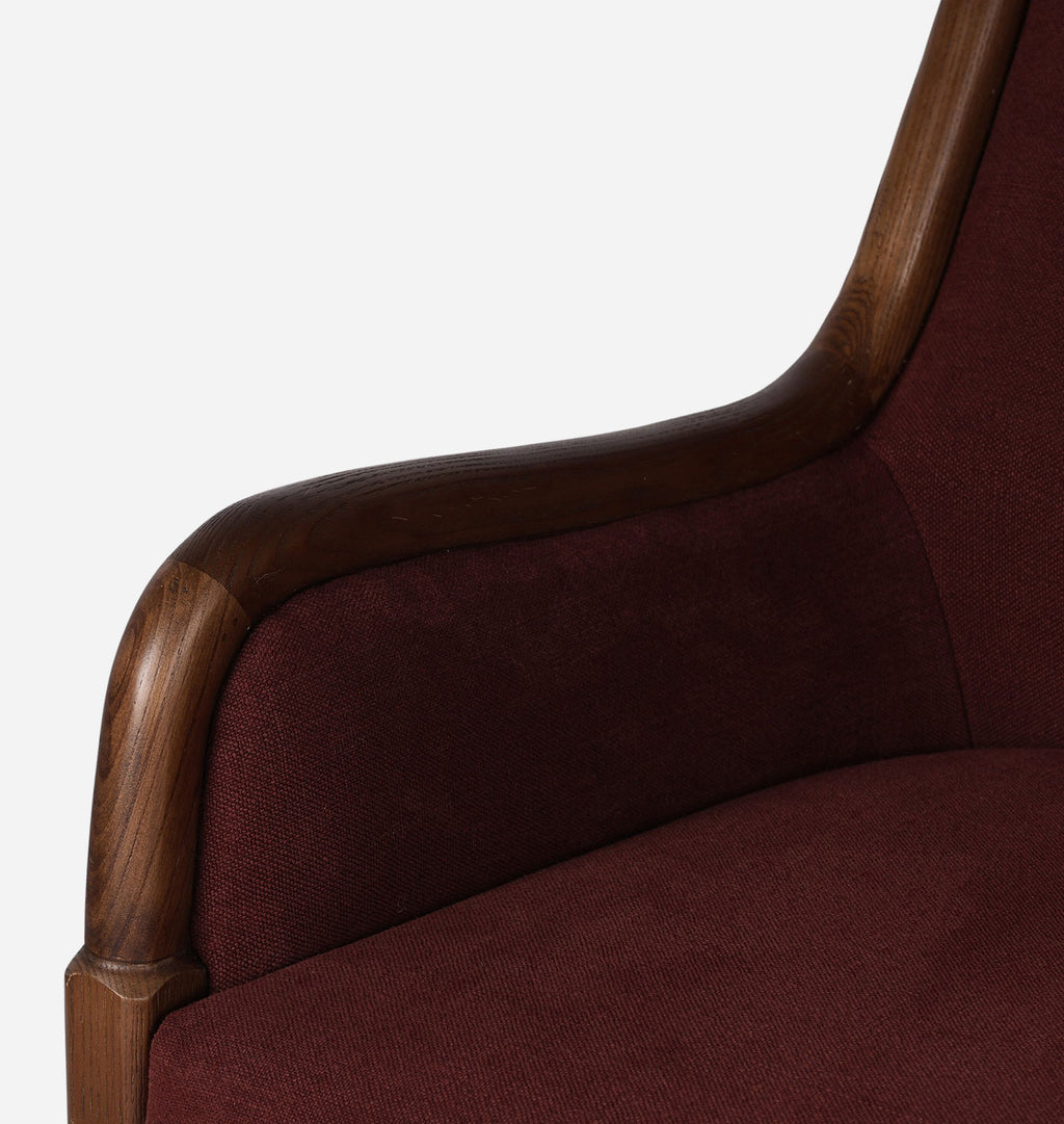 Close-up detail of an upholstered armchair showing dark burgundy fabric and a curved dark wood frame against a plain light background.