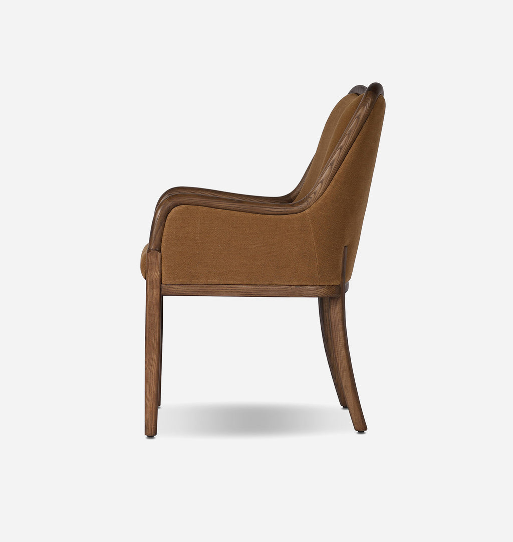 A single upholstered armchair shown from the side against a plain light gray studio background. The chair has warm camel-brown fabric upholstery with slightly darker brown trim and wooden legs.
