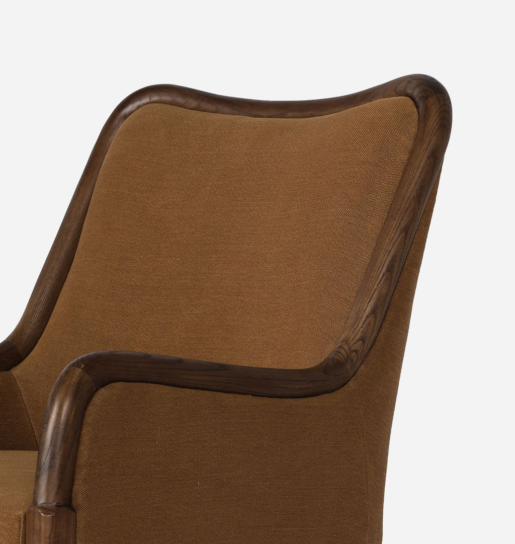 Close-up of an upholstered armchair showing the backrest and upper armrest in warm brown fabric with a dark wood frame, photographed against a light gray background.