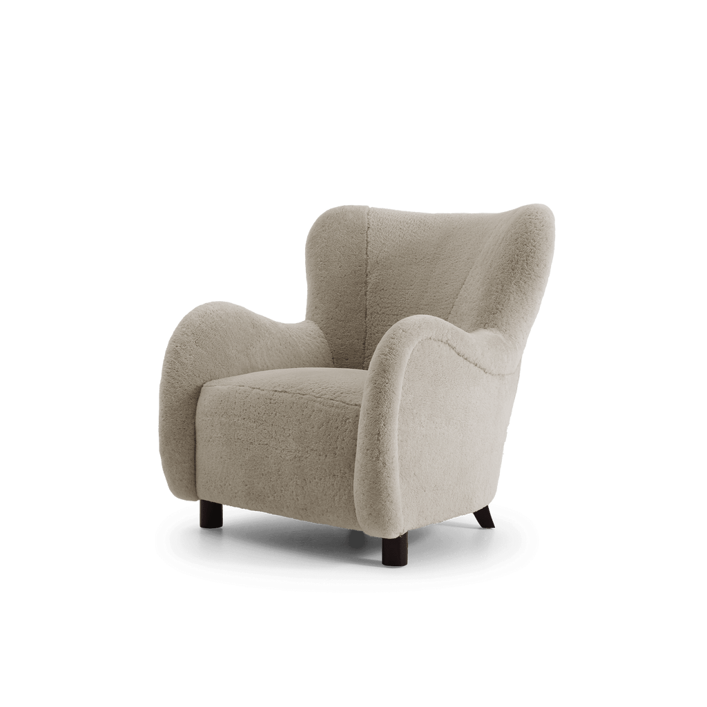 A modern low-profile armchair upholstered in a light beige shearling, featuring dark wooden legs, shown against a plain white background.