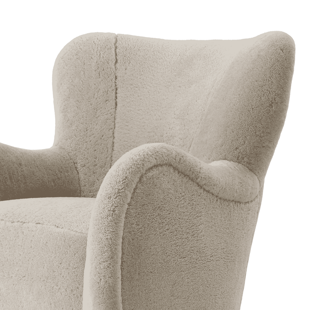 Close-up of a plush armchair upholstered in light warm gray-beige shearling, showing the backrest, armrest, and seat cushion against a plain white background.