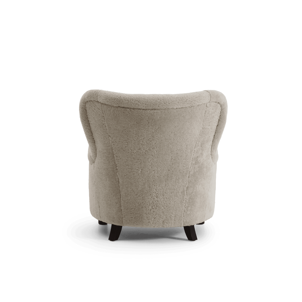 A single upholstered accent chair shown from the back, featuring light warm gray-beige shearling and dark wooden legs, isolated on a white background.