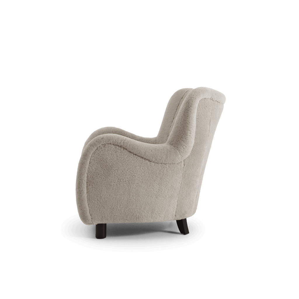 A small upholstered armchair in a light beige shearling fabric, shown from a side angle on a plain white background.