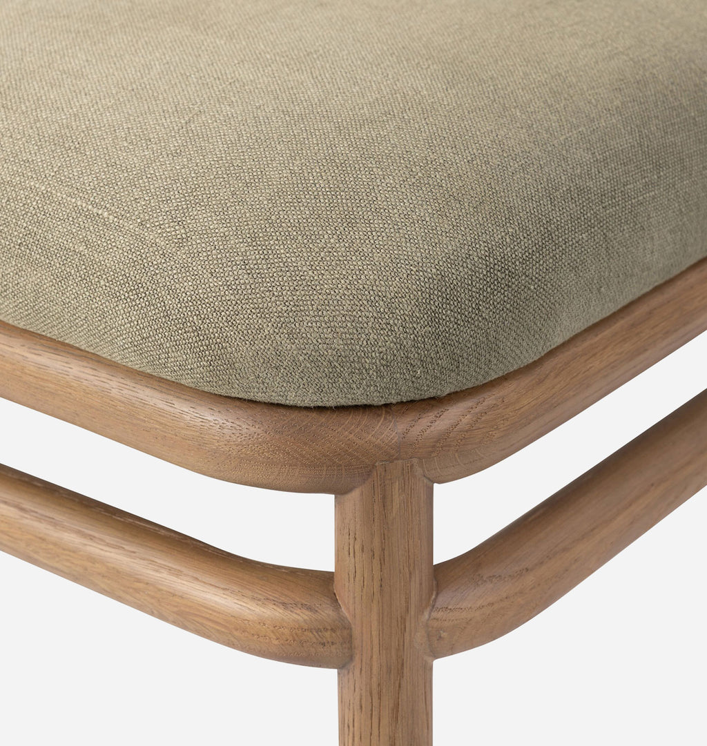 Close-up of a wooden stool or chair corner with a textured beige upholstered seat cushion and curved medium-brown wood frame on a white background.