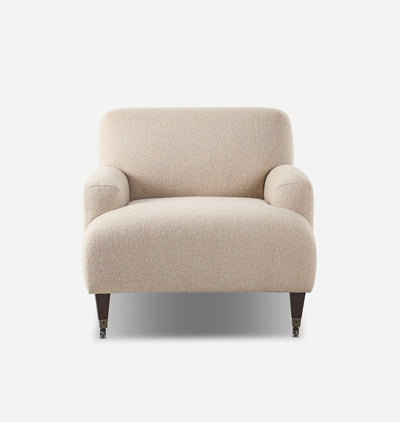A modern armchair upholstered in a textured beige bouclé fabric, featuring dark wood legs with brass casters, shown against a plain white background.