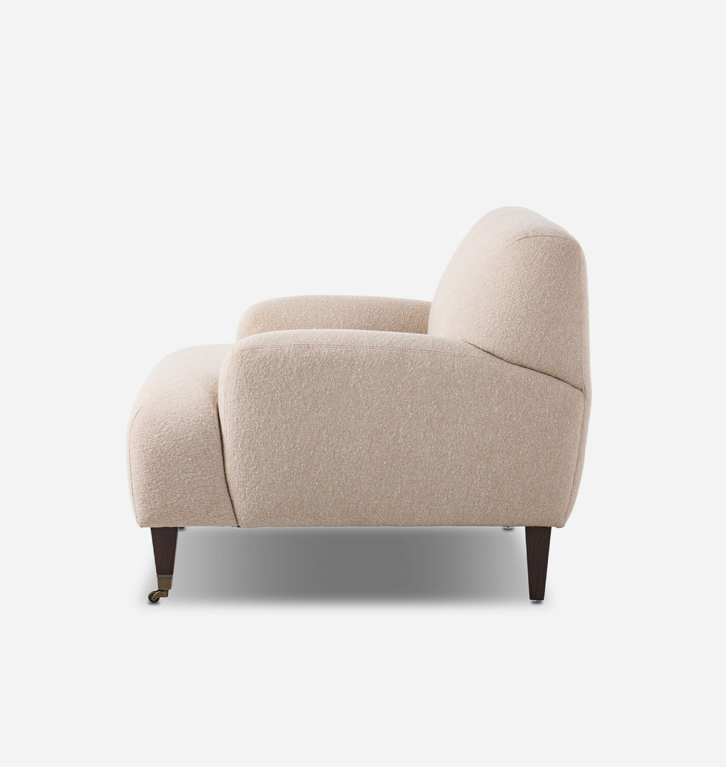 A modern beige bouclé armchair with dark tapered wooden legs, shown from a side profile view against a plain white background.
