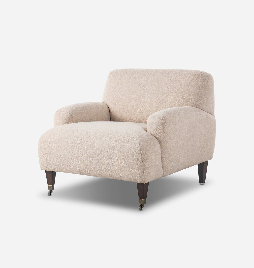 A modern beige bouclé armchair with dark tapered wooden legs and small brass casters, shown on a clean white background.