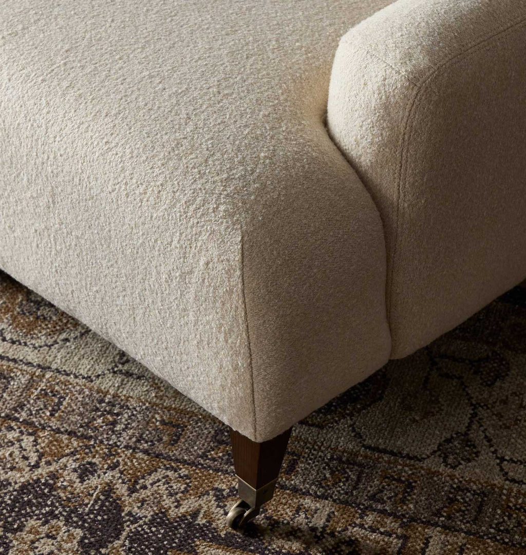 Close-up of a textured off-white upholstered furniture corner with a dark wood leg and a patterned rug underneath.