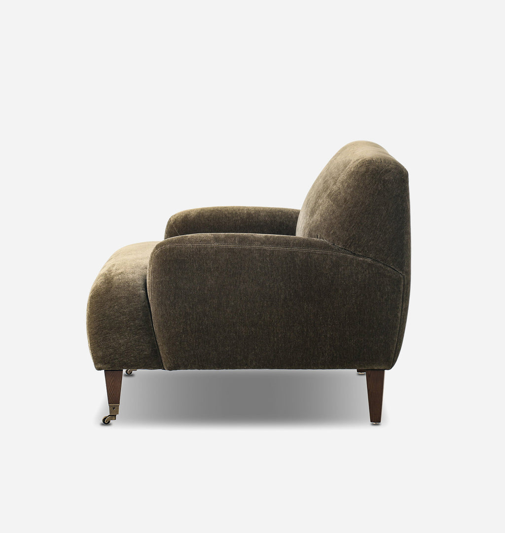 A mid-century modern armchair upholstered in textured olive-brown fabric, featuring tapered dark wood legs and a low backrest, shown from a side profile on a light gray background.