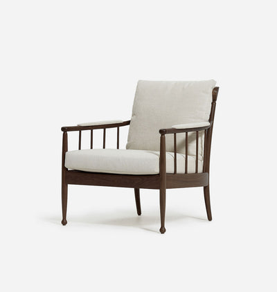 A mid-century modern armchair with a dark brown wooden frame, vertical spindles, and thick off-white textured seat and back cushions, shown against a plain white background.
