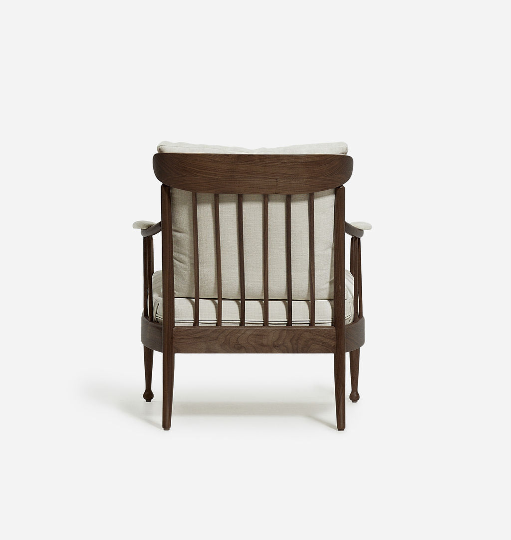 A mid-century modern armchair with a dark brown wooden frame, vertical spindles, and cream-colored cushions, shown from the back against a plain white background.
