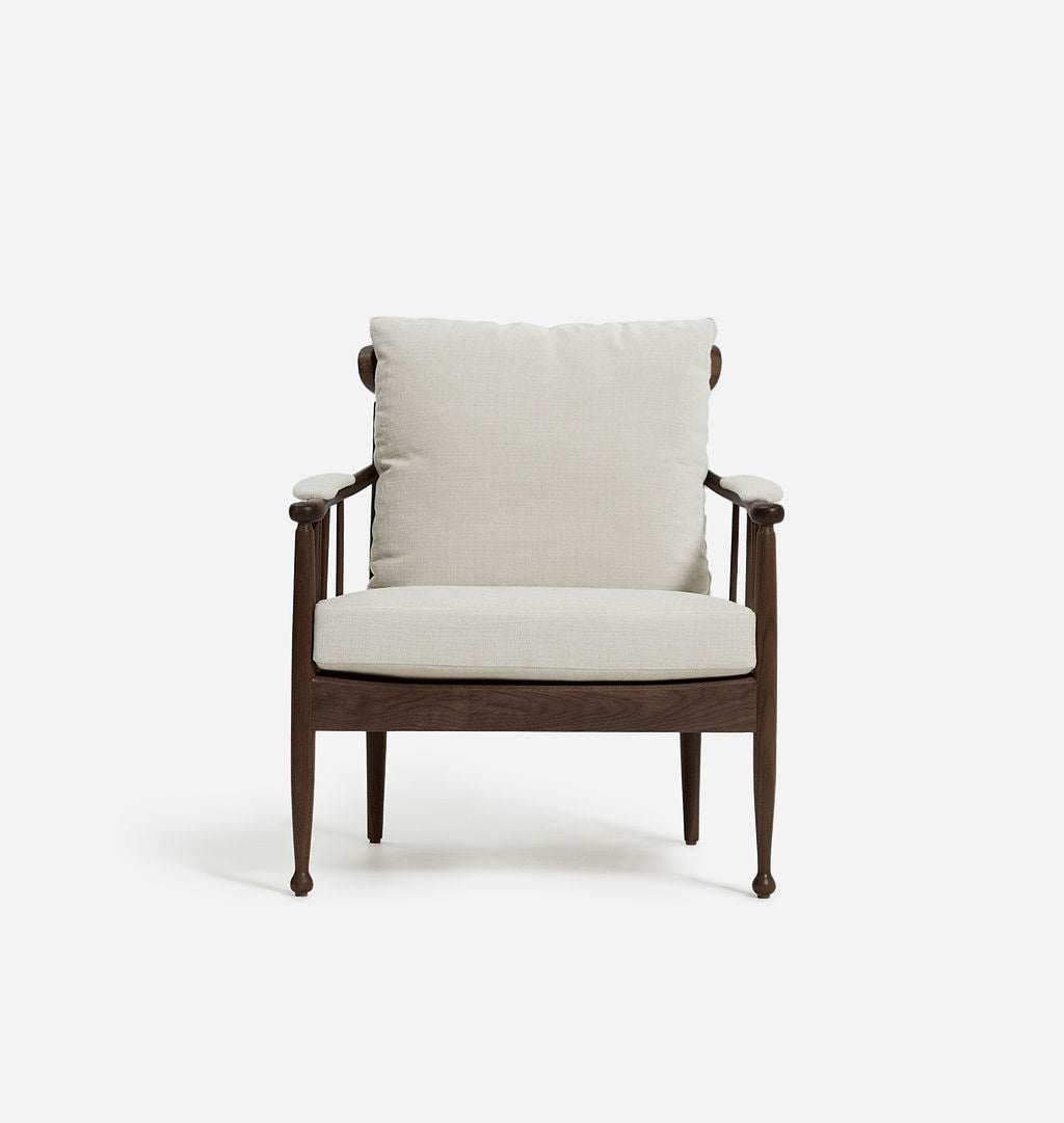 A modern accent chair featuring a dark brown wooden frame with tapered legs and curved armrests, upholstered with a light beige textured fabric cushion on the seat and backrest, set against a plain white background.