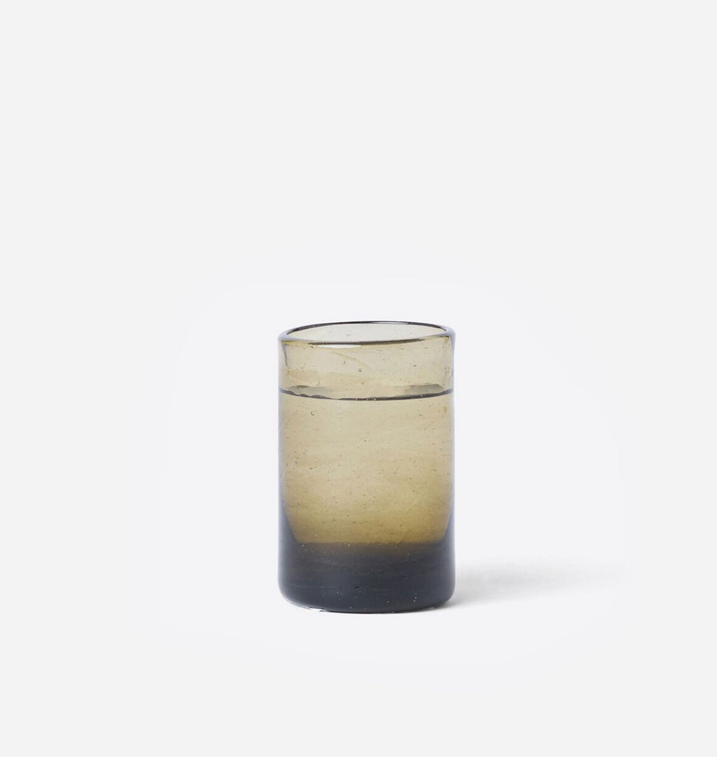 A small cylindrical glass tumbler with a gradient design, featuring a dark charcoal base that fades into a warm beige and smoky brown at the top, shown against a plain white background.