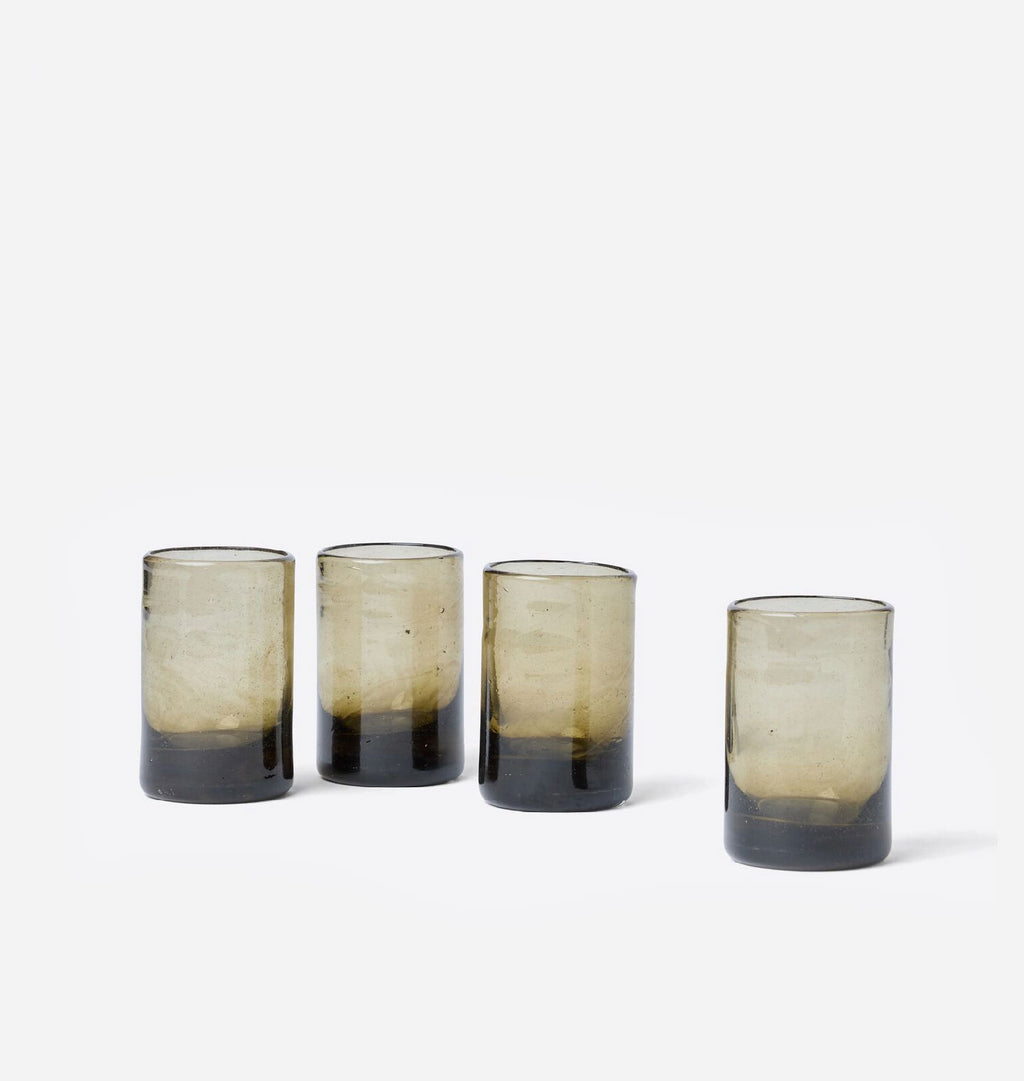 Four Murano Moyen Drinking Glass tumblers with a smoky gradient design, transitioning from a warm beige-tan at the top to a dark charcoal-black at the bottom, arranged on a clean white background.