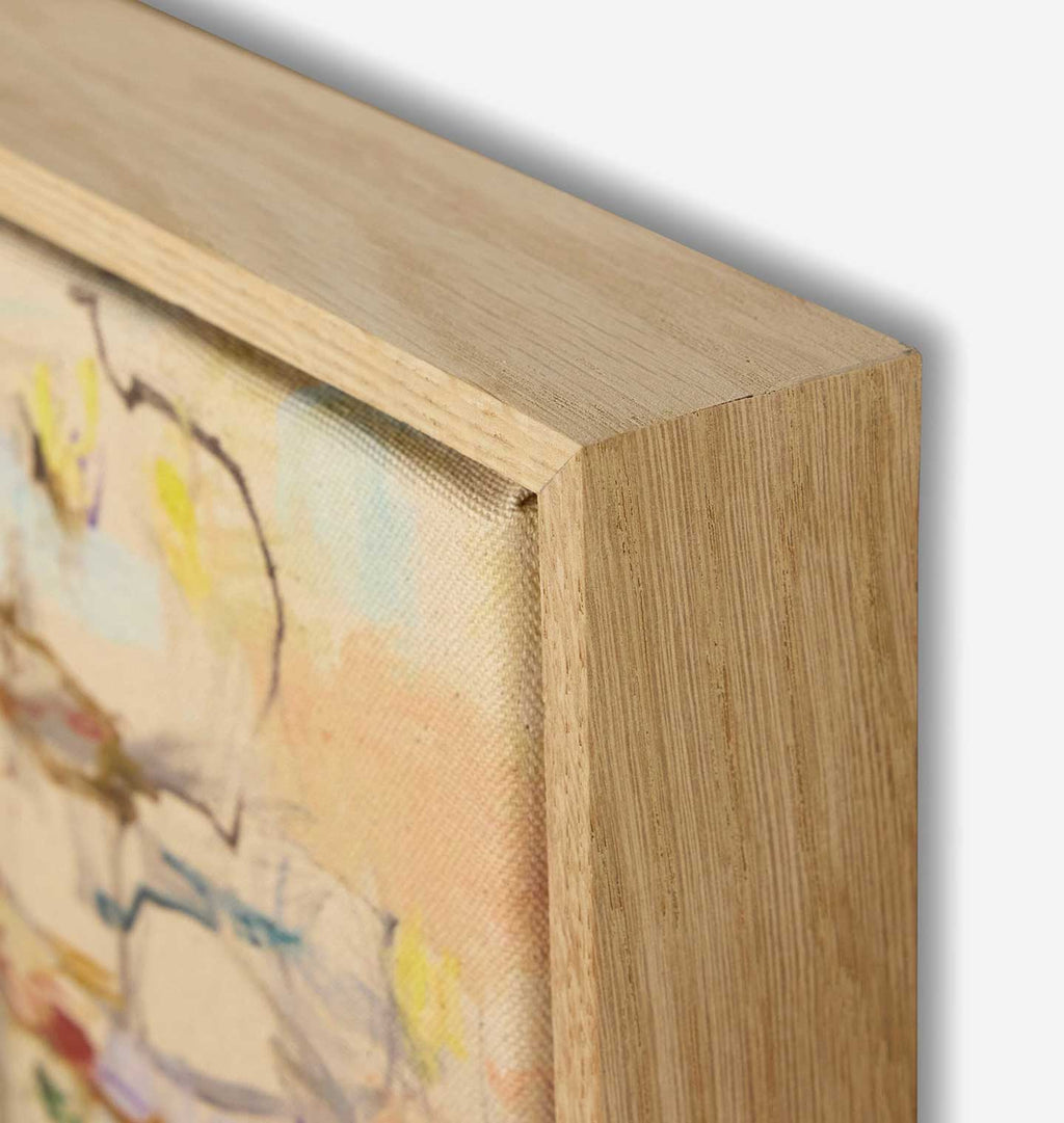 Close-up detail of a framed canvas painting showing the light oak wood frame corner and textured fabric surface with soft pastel abstract brushstrokes.