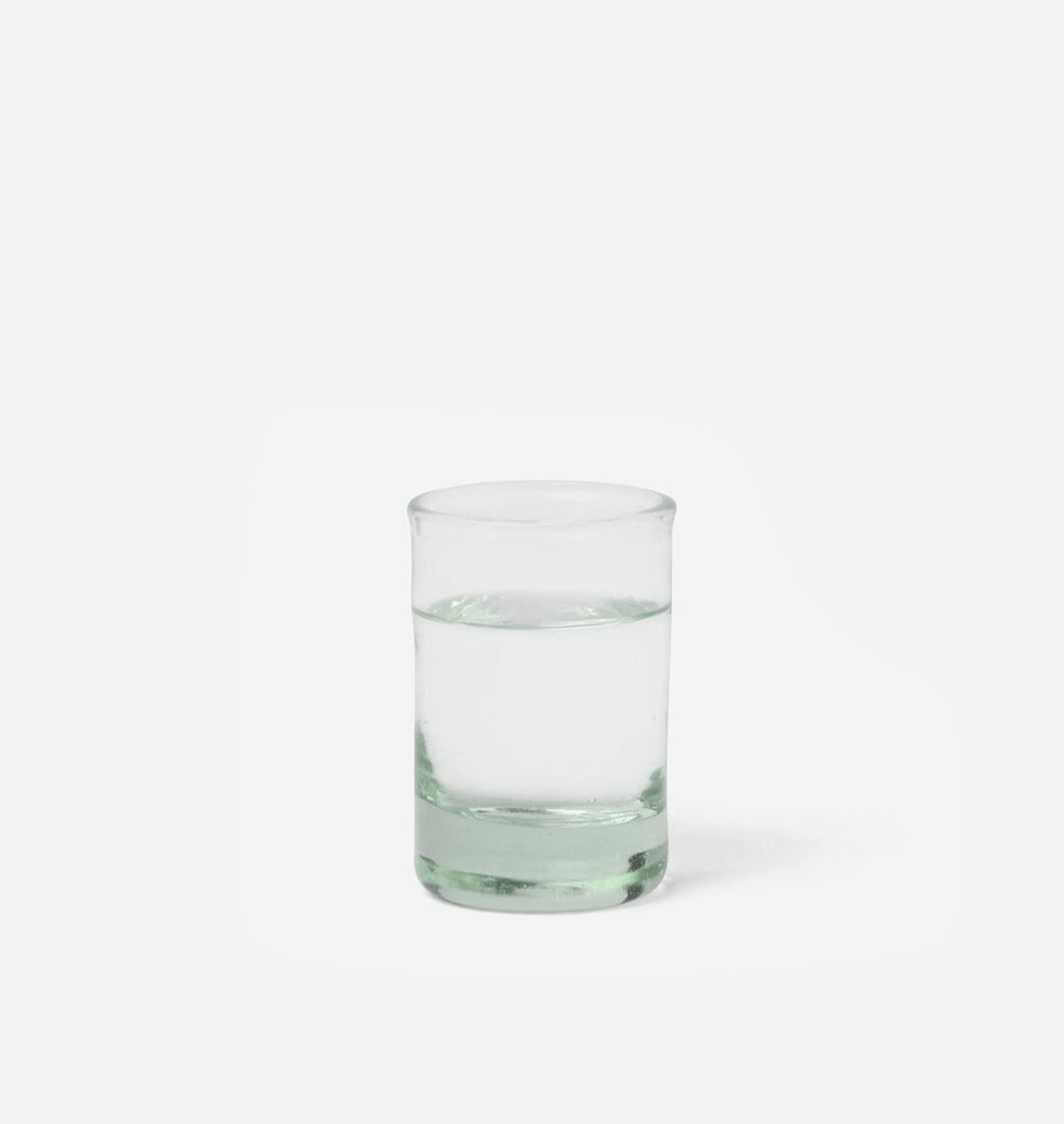 A clear glass tumbler with a thick base, partially filled with water, centered on a solid white background.