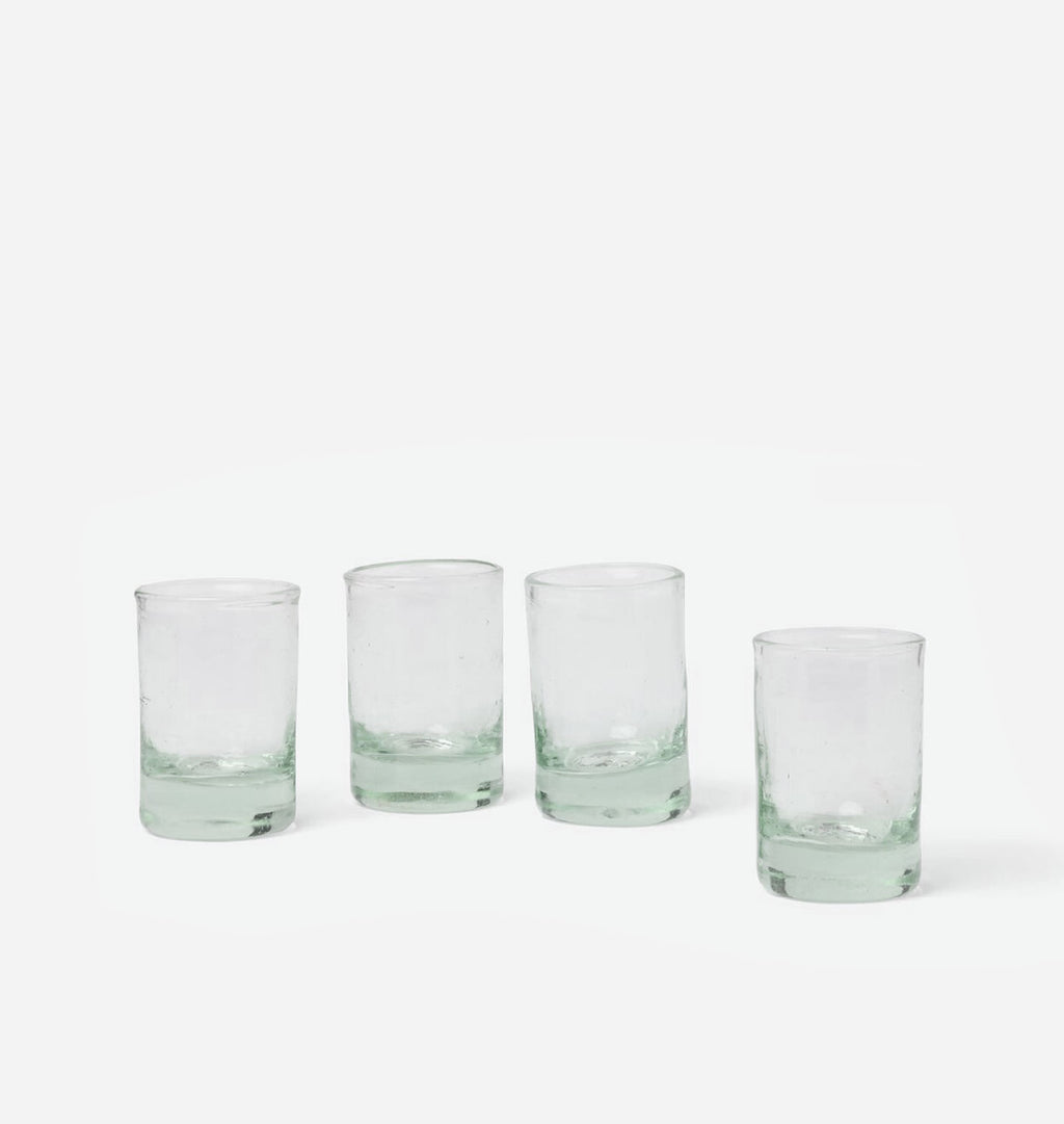 Four clear glass tumblers with a subtle pale green tint concentrated at the bases, arranged in a row against a clean white background.