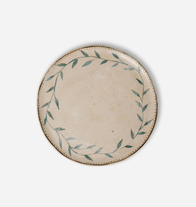 A round ceramic plate with a speckled beige center and a hand-painted green leafy wreath border, set against a plain light gray background.