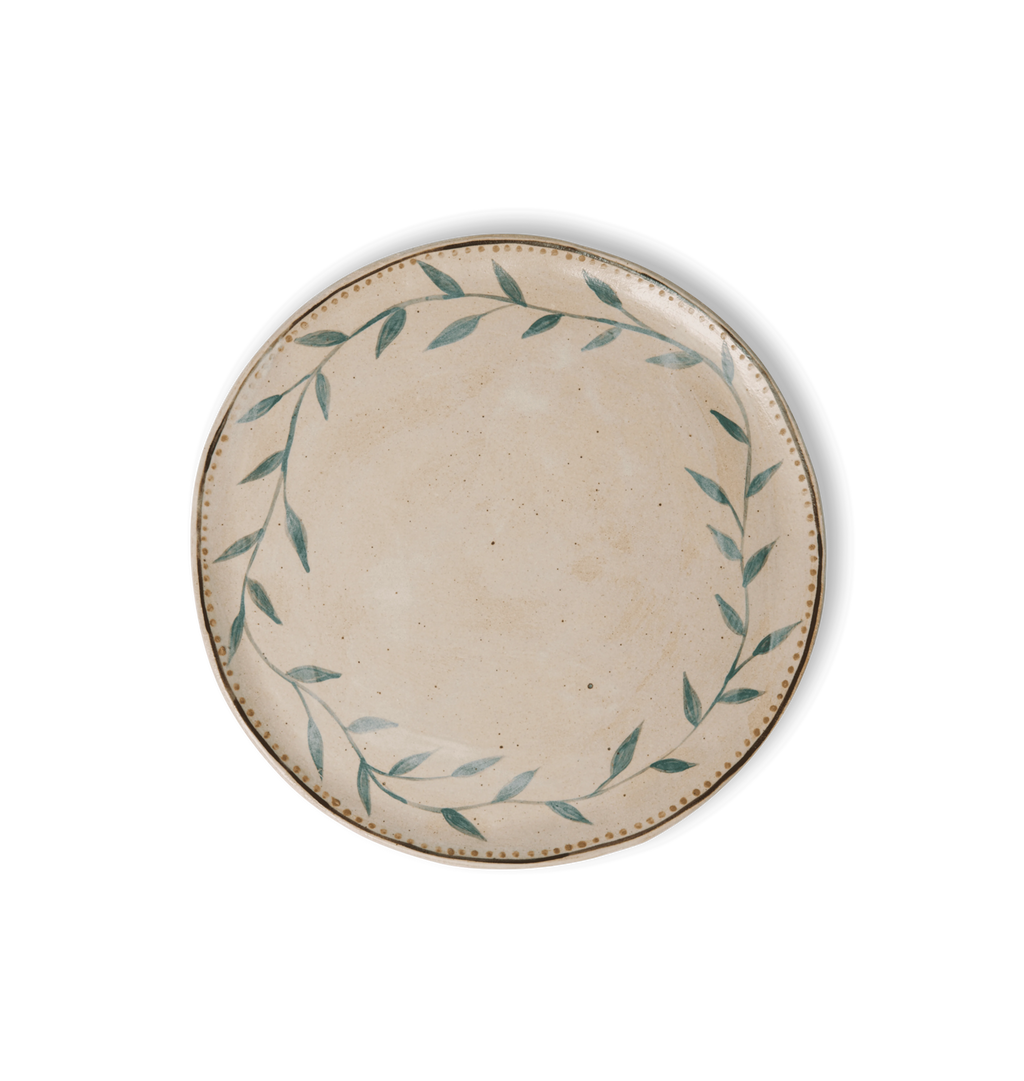 Overhead view of a round ceramic plate with an organic rim, decorated with a green leafy vine border and a gold dotted accent line on a white background
