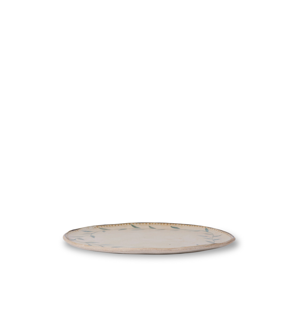 Side view of a round ceramic plate with an organic rim, decorated with a green leafy vine border and a gold dotted accent line on a white background