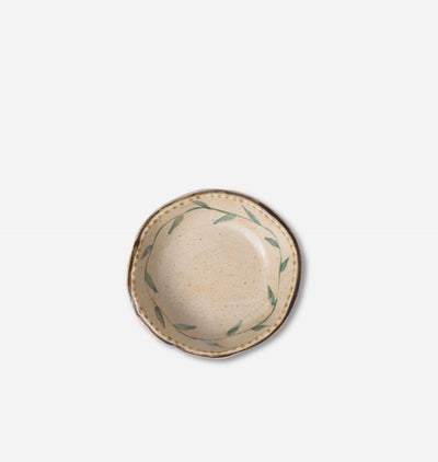 A small round ceramic plate with a scalloped rim, featuring a speckled beige interior and a delicate green leaf pattern around the edge, shown from a top-down view on a light gray background.
